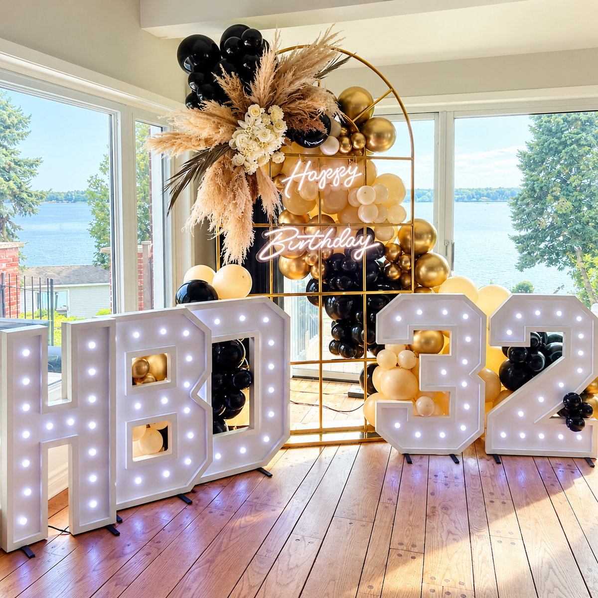 Birthday event setup with gold arch backdrop, black, gold and cream balloons, pampas florals and illuminated marquee numbers in Ottawa